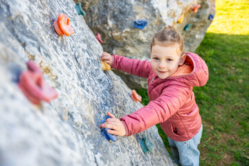 Little girl climbing an artificial climbing wall in a playground, developing strength and...