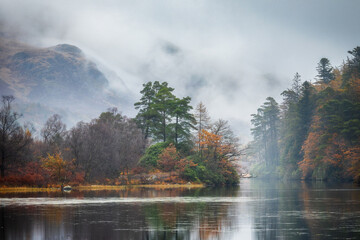 Misty moody autumn morning with colorfull trees and mountain reflecting in a lake, Loch Trool, Scotland