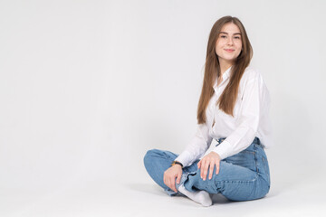 Cute young girl sitting on a floor, white background, copyspace