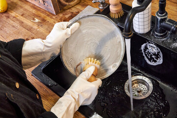 woman in white gloves washing a plate with a wooden brush, eco-friendly cleaning close-up of hands