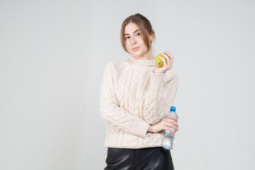 Attractive positive young girl in beige sweater with bottle of water posing standing on white...