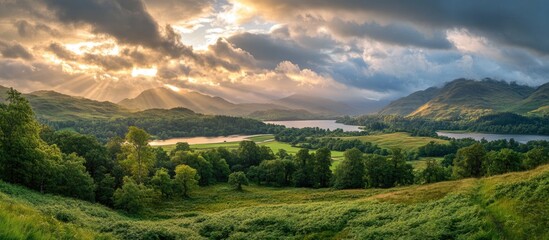 Obraz premium Serene panoramic view of lush green landscape with dramatic clouds, sun rays breaking through and reflecting on a tranquil lake.