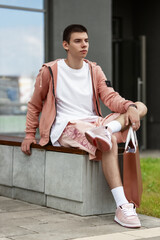 young man posing in trendy summer clothes with bag on street on sunny day, concept of trendy urban summer clothes, youth trend