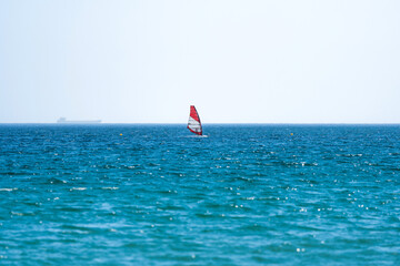Windsurfer gliding over the blue sea in Tarifa, Spain, on a sunny day with a cloudy sky and a cargo...