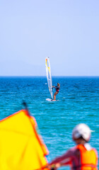 Young woman with her hair up windsurfing in the ocean in Tarifa, Spain, on a sunny day with another...