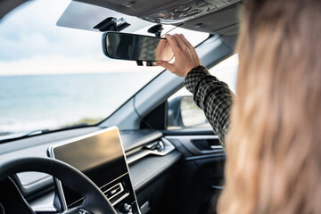 Backside view of an unrecognizable woman adjusting the rearview mirror in her car before driving....