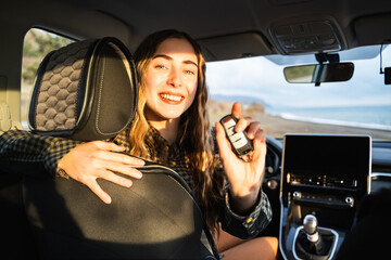 A young white woman holding a key of her new modern car. Happy smiling female owner of new...