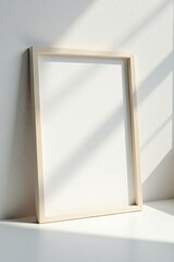 A simple, light beige frame rests against a bright white wall, bathed in the soft glow of sunlight casting gentle shadows