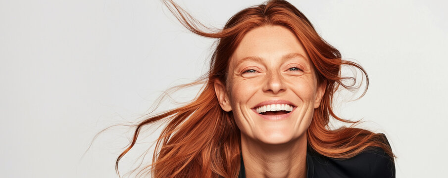 Studio portrait of happy laughing redhead woman with windblown red hair, white background