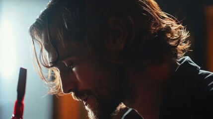 Male hairstylist focused on cutting hair with red razor in profile view illuminated against a blurred background showcasing artistry in barbering.