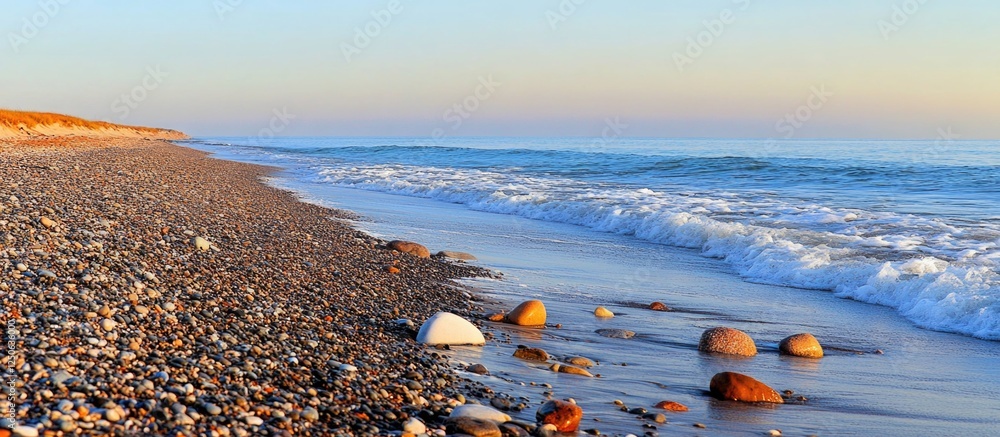Aufkleber Rocks on a tranquil beach with gentle waves lapping at the shoreline during a serene sunset.