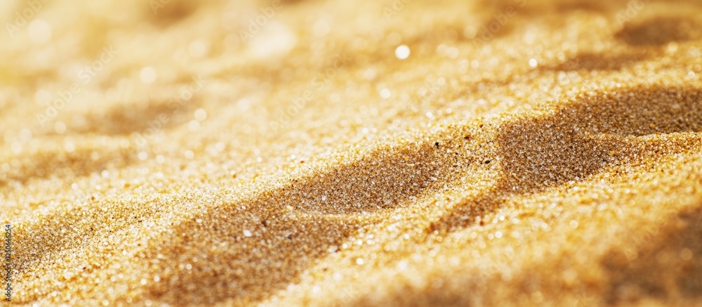 Poster Golden sand texture on a beach with ripples and sunlit reflections creating a warm and inviting coastal atmosphere.