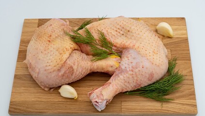 Fresh raw chicken legs with dill and garlic on a wooden board.