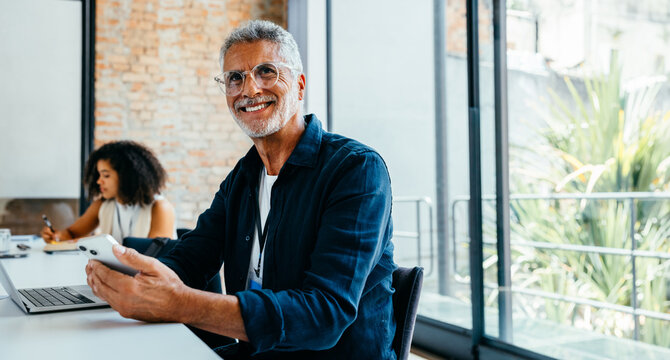 Grey-haired businessman using technology in a contemporary office setting, smiling confidently while using modern technology