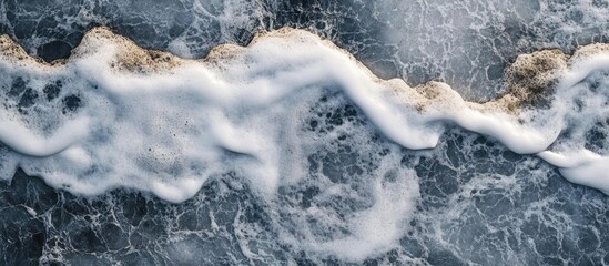 Obraz premium Aerial view of waves crashing on rocky shore creating textured abstract patterns in deep blue and white tones for background use