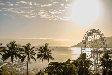 Golden hour over the ferris wheel, treetops, lagoon and hilly backdrop of Cairns Esplanade - Coral...