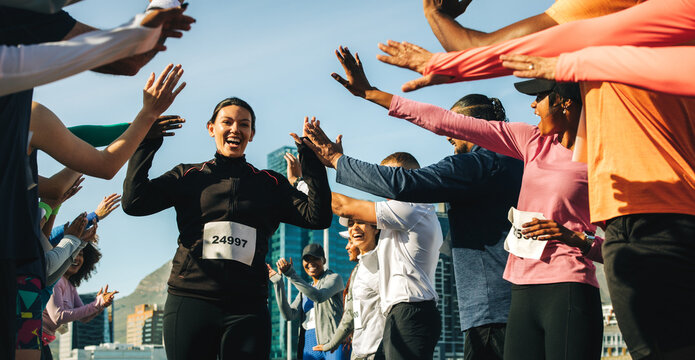 Happy female runner celebrates as crowd cheers during outdoor marathon