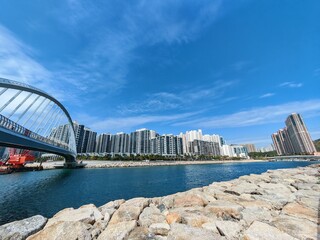 Hong Kong, Tseung Kwan O waterfront view with modern apartments and houses under a bright blue sky. A bridge is visible on the left side.