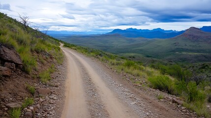 Winding dirt road meandering through the green hills and mountains under a cloudy sky : Generative AI