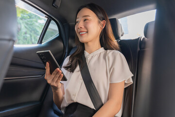 Smiling Asian woman is sitting in a private car and is holding a phone and looking outside.