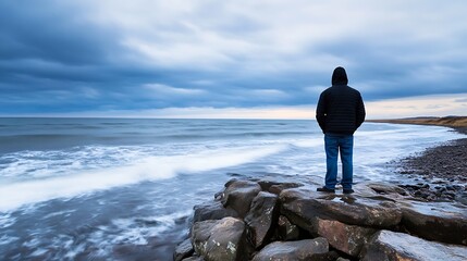 Man standing on rocky shore staring at the vast ocean under a moody cloudy sky looking contemplative : Generative AI