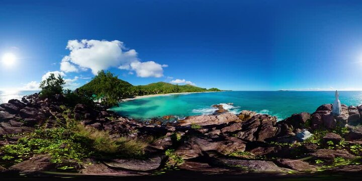 A vibrant coastal scene with rocks, clear waters and green hills extending along the shoreline under a bright sky. Praslin, Seychelles. Constance Lemuria Beach. 360 Degree view.