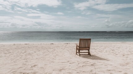 A solitary wooden chair on a tranquil beach facing the calm ocean under a cloudy sky