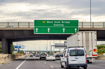 Traffic flows beneath a directional sign on Melbourne's West Gate Bridge approach, showing exit...