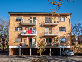 A classic three-story brick apartment building with balconiesl and a ground-floor parking garage. A symmetrical design typical of mid-century Australian residential complex.