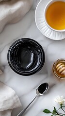 Top view, black jar filled with thick shiny shilajit resin, with a spoonful of resin next to it and a cup of tea, shot under soft lighting to give a natural look.