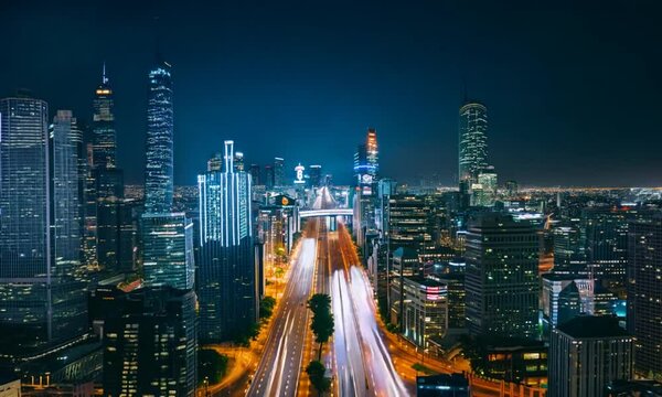 Timelapse shot of a city skyline at night, with skyscrapers glowing brightly and traffic lights streaking across the roads. The scene transitions from night to dawn, showcasing the city's tr
