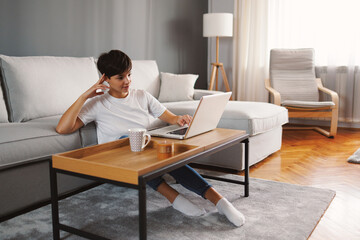 Freelancer working remotely from home enjoying a cup of coffee while using laptop on a wooden table