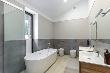 The interior of a bathroom with a window in a private house. The decor is made in light gray tones.