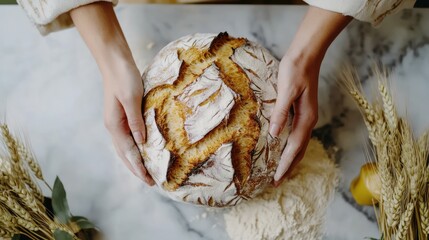 Hands Holding Freshly Baked Artisan Bread on Marble Surface Surrounded by Wheat and Flour for Rustic Cooking