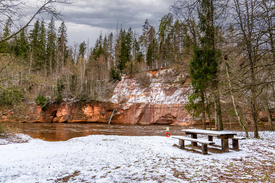 Winter Riverside Picnic Spot with Sandstone Cliffs. Serene Nature Retreat with Red Cliffs and Snowy Ground. - Powered by Adobe