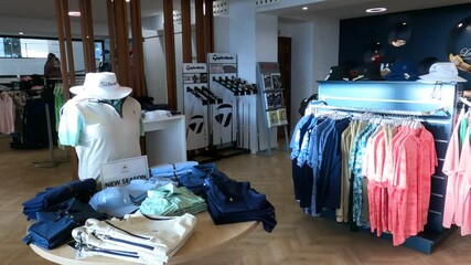 Golf pro shop interior featuring clothing racks, mannequins, golf clubs, and accessories on display. Bright and modern retail space.
