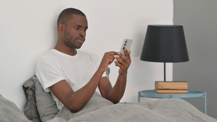 African Man Using Smartphone while Sitting in Bed