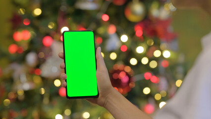 Woman Holding Phone with Green Screen in Front of Decorated Christmas Tree