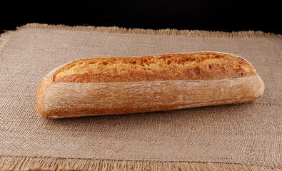 Baguette, a loaf of bread lies on a burlap napkin. Side view.