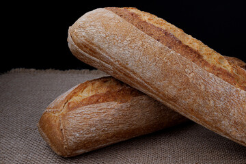 Two loaves of baguette lie on a burlap napkin. Two crossed baguettes.