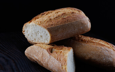 Fresh hot bread. Two loaves of baguette on a black background. Sliced bread. Art bread.