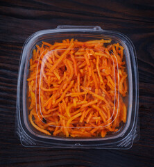 Korean spicy carrot salad in a sealed plastic container. Top view.