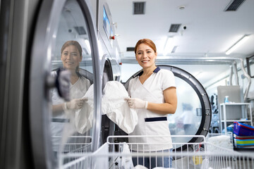 Professional laundry washing and drying service. Female worker standing by washing machine and...