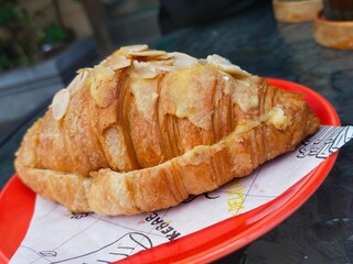 Almond Croissant on red plate over the glass table. Sweet french pastry baked croissant with almond flakes