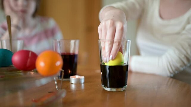 Two big sisters and their little brother dyeing Easter eggs at home. Children painting colorful eggs for Easter hunt. Kids getting ready for Easter celebration. Family traditions. Slow motion footage.