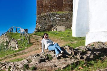Latin brunette woman, young and beautiful is casually dressed and sitting on a big stone in the...