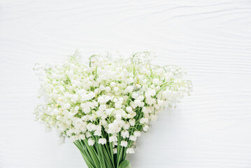 delicate bouquet of lily of the valley flowers with lush green stems placed on a white wooden surface, creating a soft and elegant spring composition