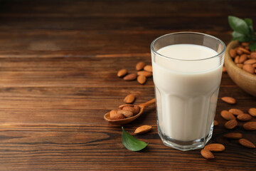 Fresh almond milk in glass and nuts on wooden table, space for text