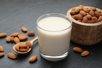 Fresh almond milk in glass, spoon and nuts on black table, closeup