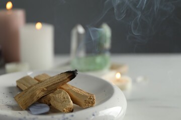 Smoldering palo santo stick and gemstone on table, closeup. Space for text